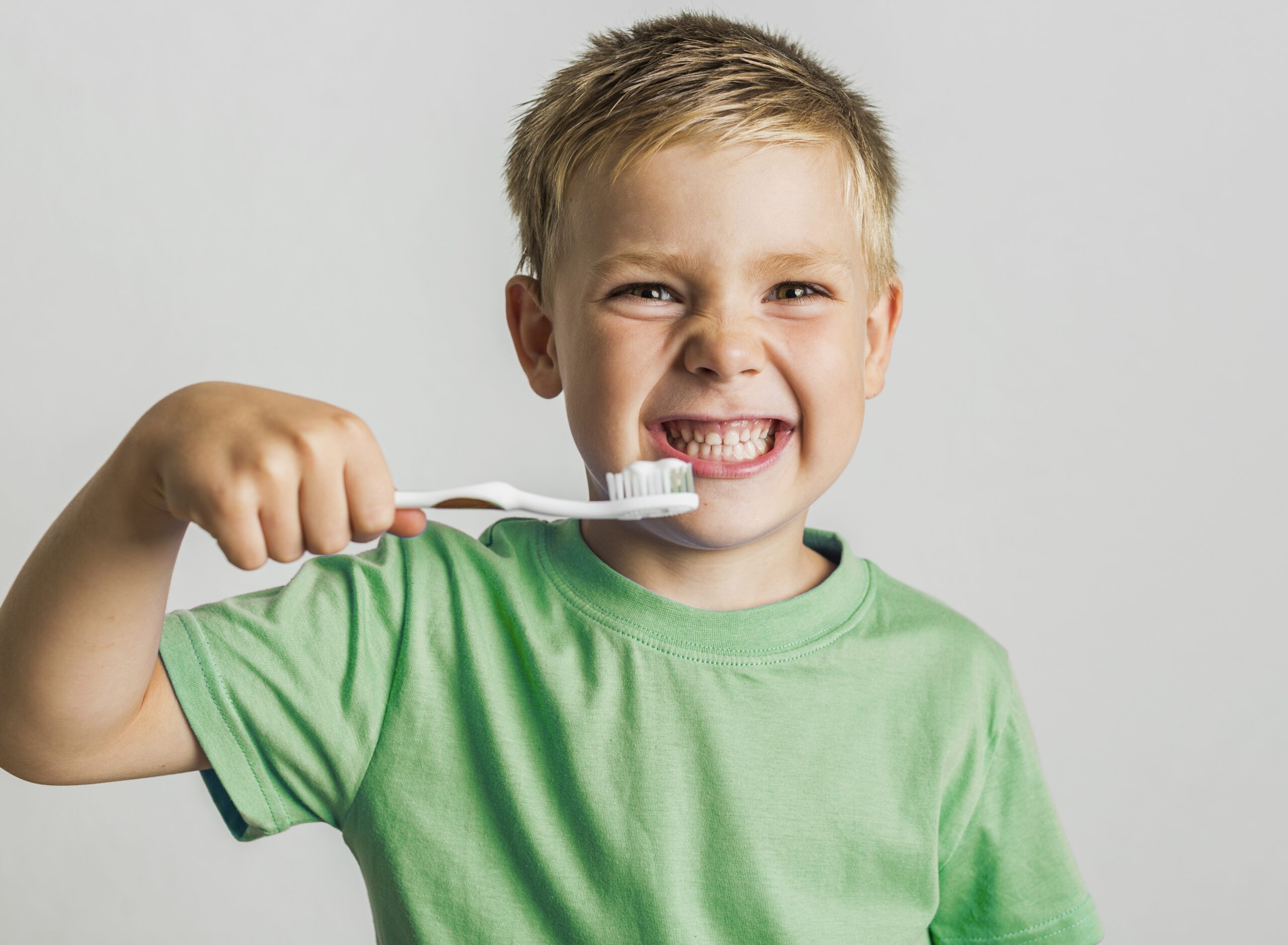 Young boy smiling while brushing his teeth with a toothbrush during pediatric dental care at Revive by OrthoSports